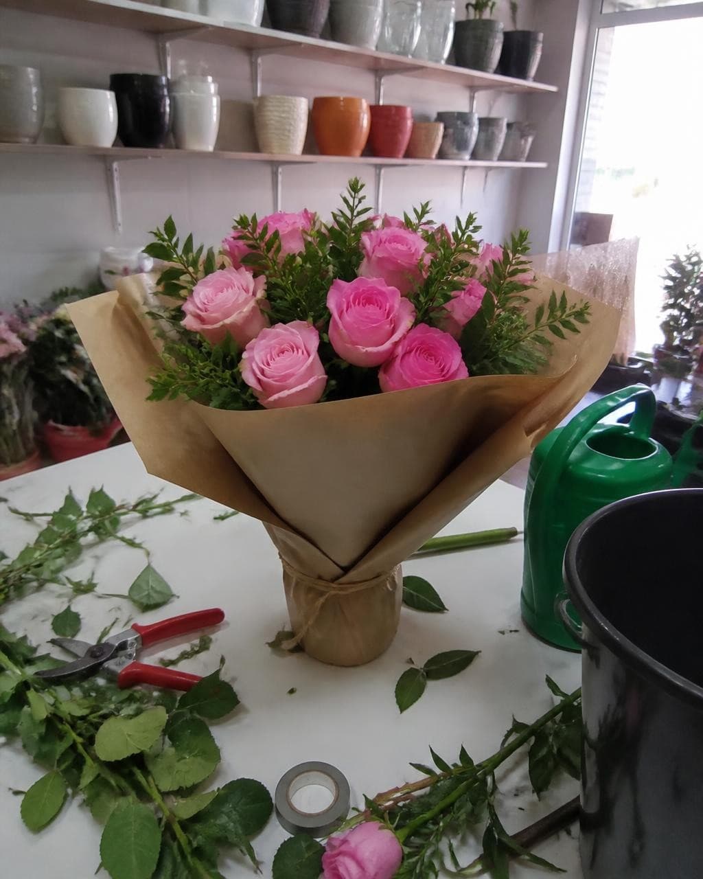 A foto crua de celular do buquê no balcão da floricultura, com a bagunça do serviço em volta